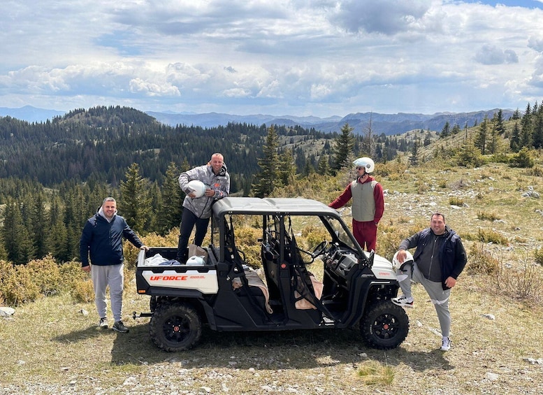 A group of people standing around a UFORCE ATV in a mountainous area with trees and hills in the background. 1