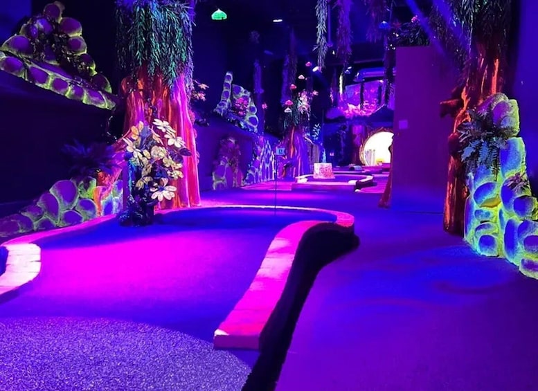 A brightly lit indoor pathway with artificial plants and colorful lighting. 2