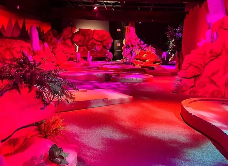 A dimly lit indoor exhibit with red lighting, featuring a central pathway, rock formations, and artificial foliage. 4
