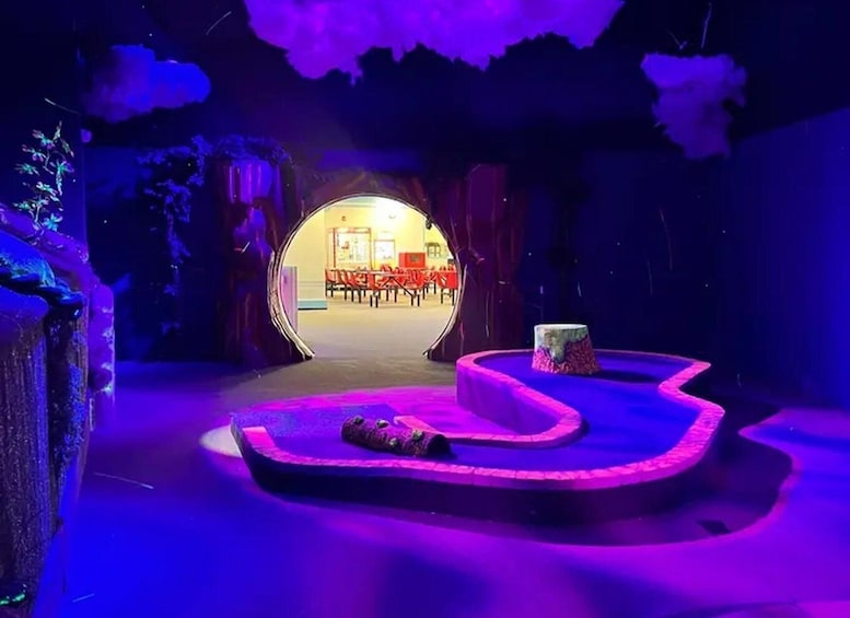 An indoor stage with a circular platform, a tree stump, and a view of an outdoor area with chairs and tables. 1
