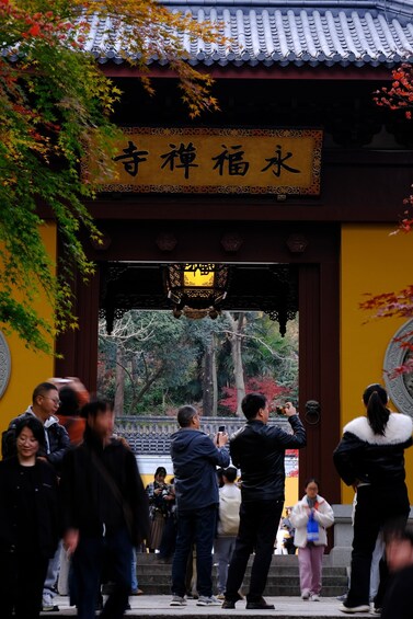 A traditional Japanese gate with a sign, surrounded by people and autumn foliage. 2