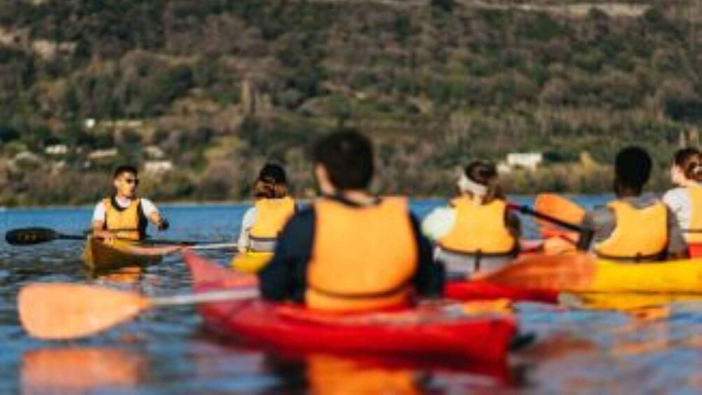 A group of people kayaking on a calm body of water with a hilly landscape in the background. 2