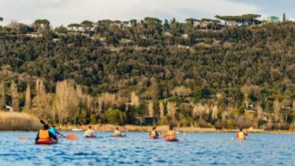 People kayaking on a calm body of water with a forested hillside in the background. 3