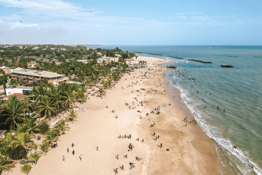 A beach with people, palm trees, and buildings along the shore. 1