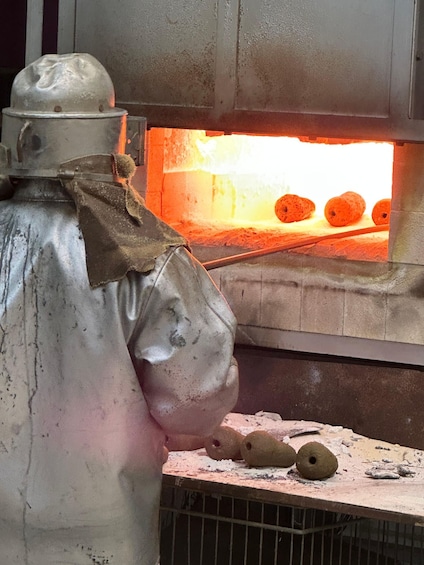 A person wearing a protective suit near a brick oven with glowing embers. 1
