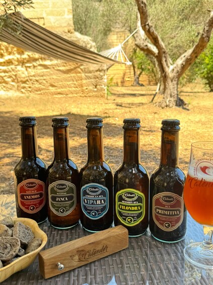 Six beer bottles and a glass of beer on a table outdoors. 5