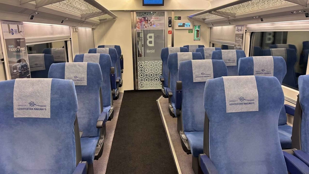 A train carriage with blue seats, a central aisle, and overhead luggage compartments. 3