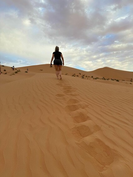 A person walking on a sandy dune with footprints, under a cloudy sky. 4