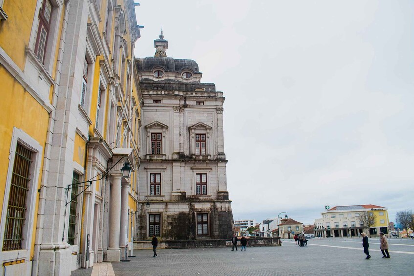 A historic building with classical architecture, a paved square, and a few pedestrians. 5