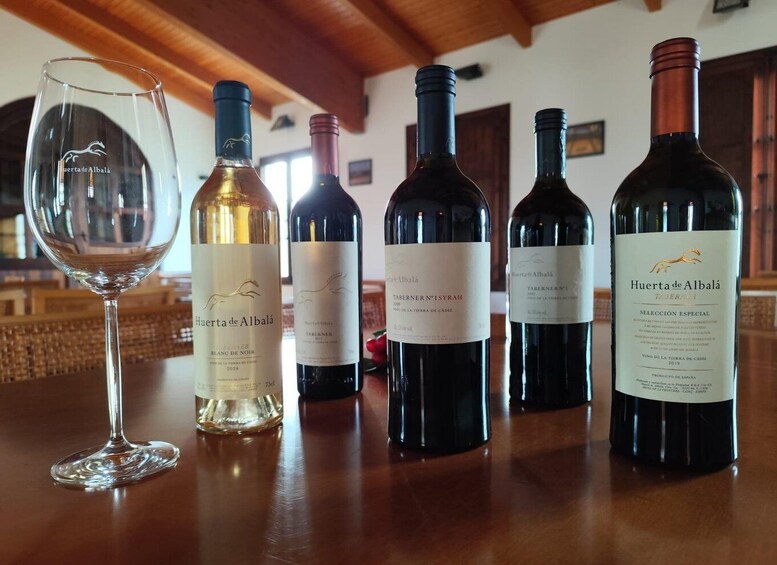 A wine tasting event with several bottles of Huerta de Albala wine and a glass of white wine on a wooden table. 1