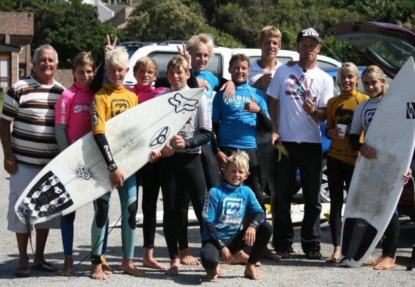 A group of people with surfboards, standing on a beach with cars in the background. 2