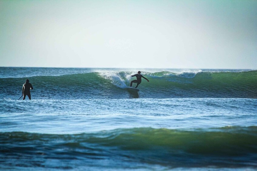 A surfer riding a wave in the ocean with another person standing nearby. 5