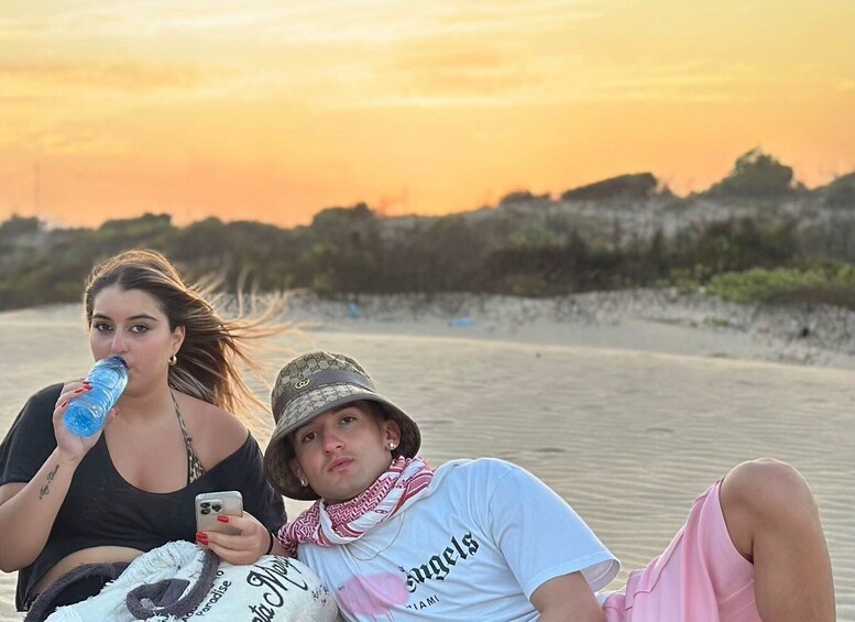 Two people sitting on a sandy beach with a sunset in the background. 3