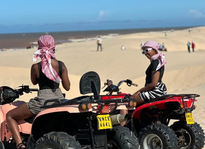 Two people on ATVs on a sandy beach with a clear sky. 4