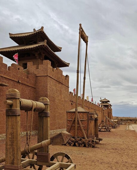 A historical reenactment site with wooden structures, a drawbridge, and wheeled carts. 2