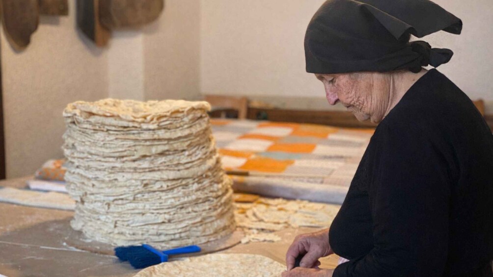 A person preparing food, specifically cutting dough, with a large stack of dough nearby. 3