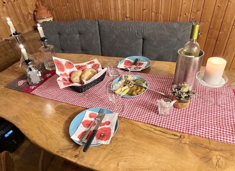A wooden dining table with a red and white checkered tablecloth, plates with food, candles, and a bottle of wine. 3
