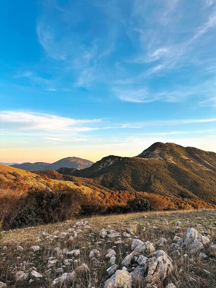 A mountainous landscape with autumn foliage, rocky terrain, and a clear sky. 1