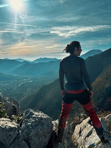 A person standing on a rocky outcrop overlooking a mountainous landscape with a clear sky. 2