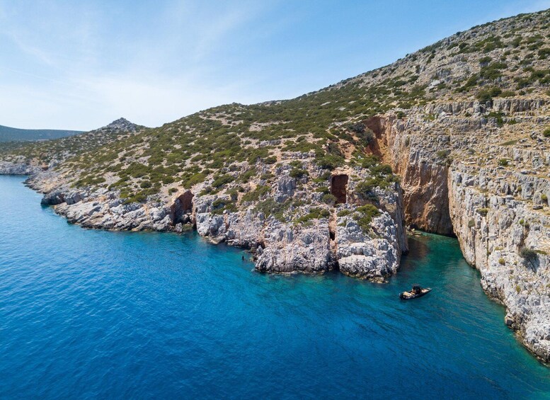 A coastal landscape with rocky cliffs, clear blue sea, and sparse vegetation. 4