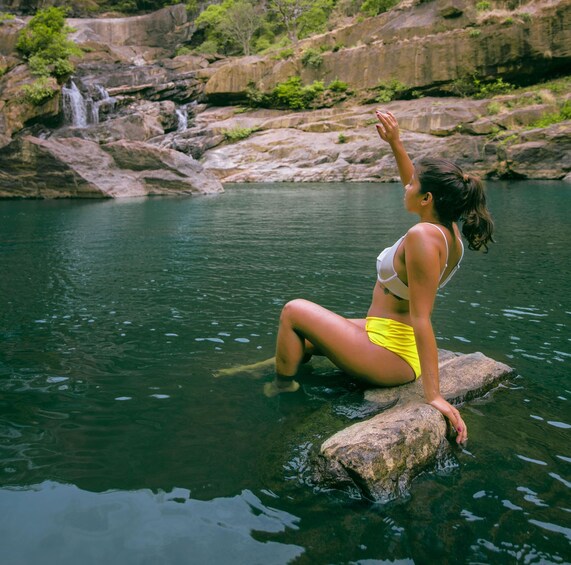 A person sitting on a rock by a waterfall in a natural setting. 1