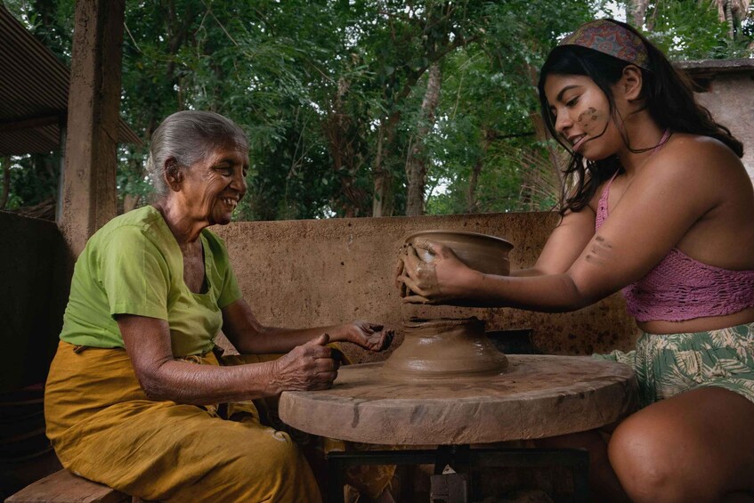An elderly person teaching pottery to a younger individual. 4