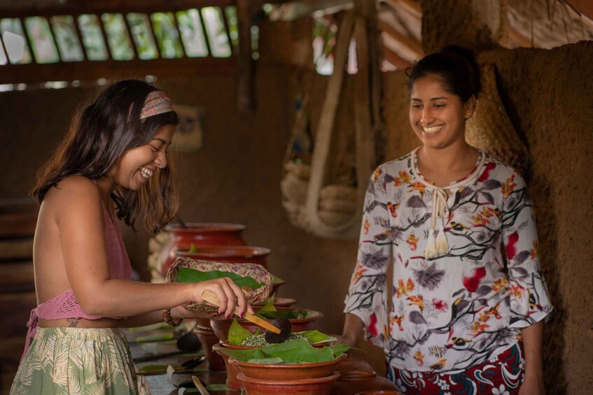 Two individuals engaged in a traditional activity involving terracotta pots and green leaves. 5