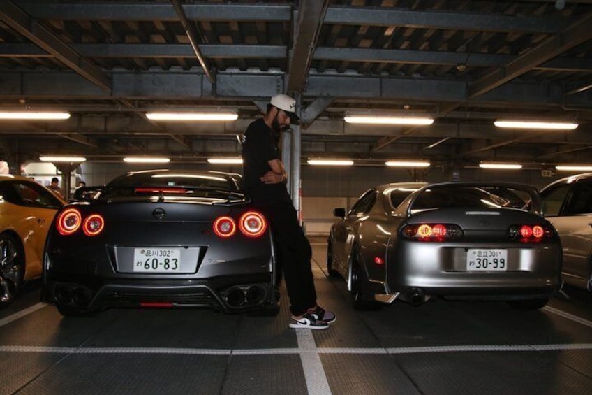 A person standing between two sports cars in a parking garage. 4
