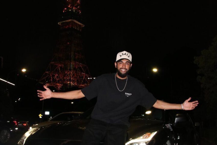 A person standing next to a car with a tower in the background. 2