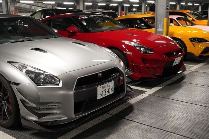A parking garage with several sports cars, including a silver and a red one. 1