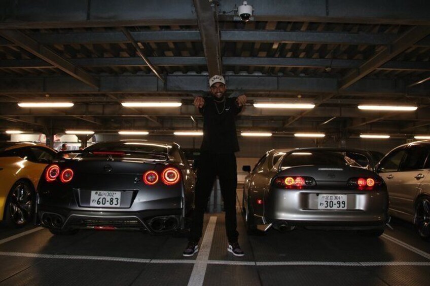 A person standing between two sports cars in a parking garage. 5