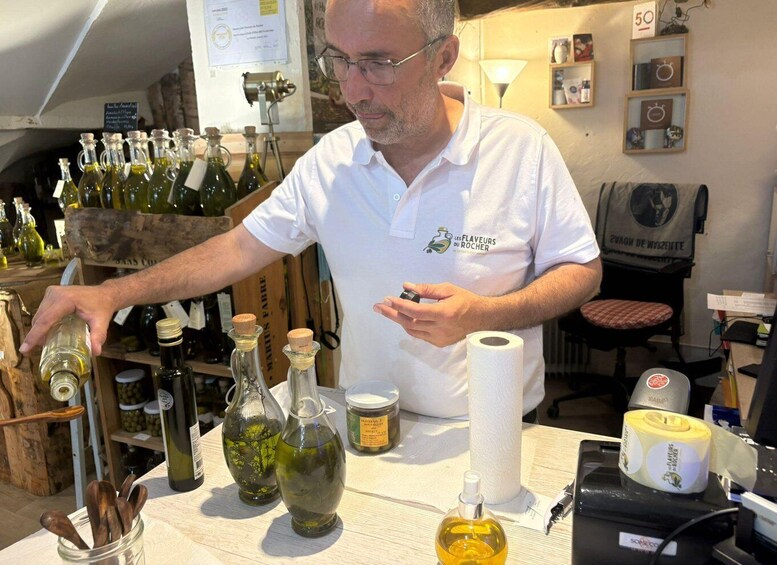 A man in a white shirt with a logo, standing at a table with various bottles and containers, likely in a winery or distillery setting. 4