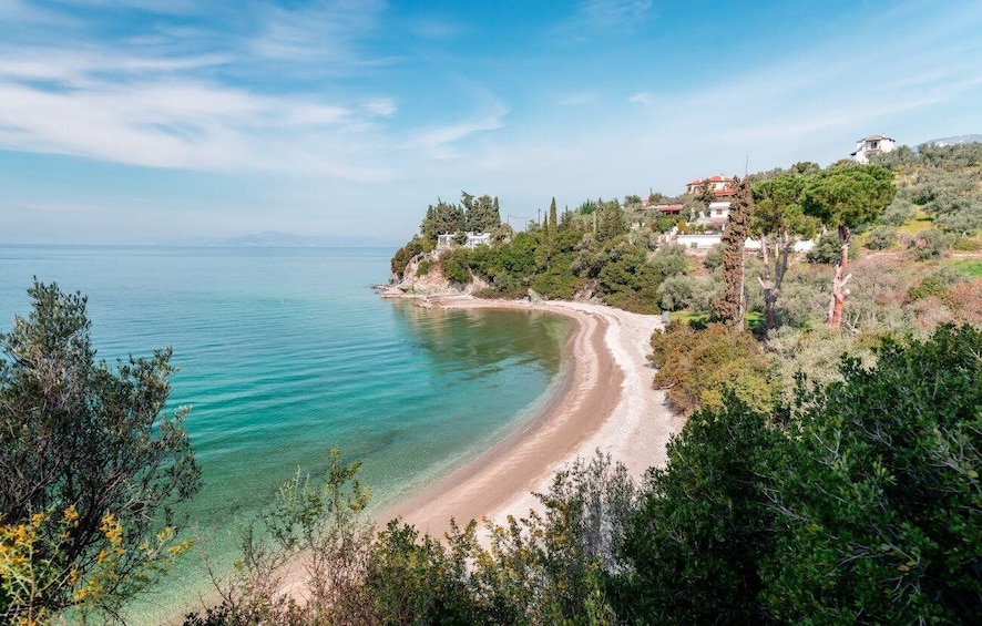A coastal landscape with a sandy beach, clear turquoise waters, and a backdrop of hills with scattered buildings. 1