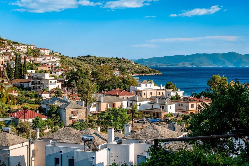 A coastal town with white buildings, a clear blue sky, and a view of the sea and distant mountains. 3