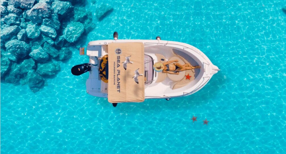 A boat with a 'SEA PLANET' sign on a turquoise sea with rocks. 5
