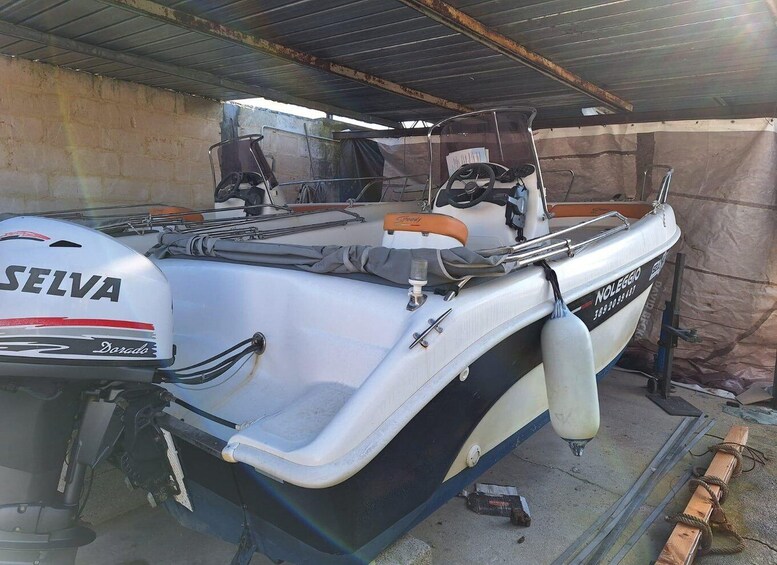 A boat with a white hull and a black trim, equipped with a 'SELVA' outboard motor, a 'NOLEGGIO' brand steering wheel, and various fishing gear. 4