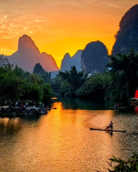 A river with boats, a person rowing, and mountains in the background. 1