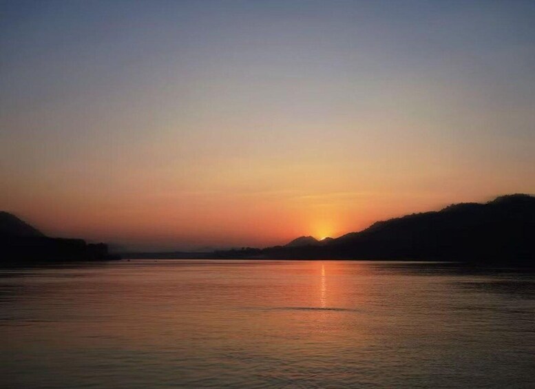 A sunset over a calm river with hills on either side. 2