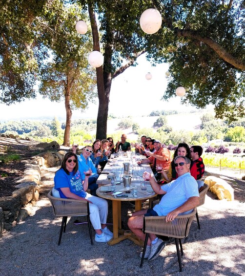 A group of people seated around a round table outdoors, enjoying drinks and conversation. 3