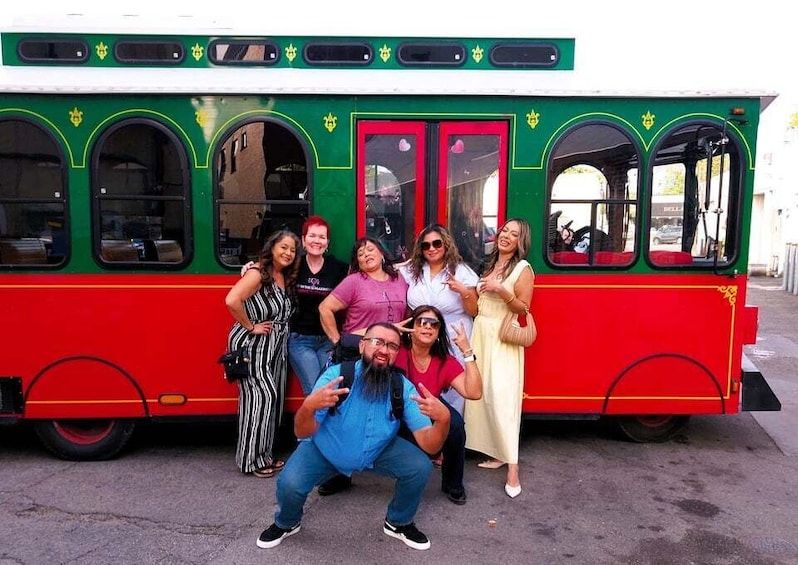 A group of people posing in front of a red and green tram. 1