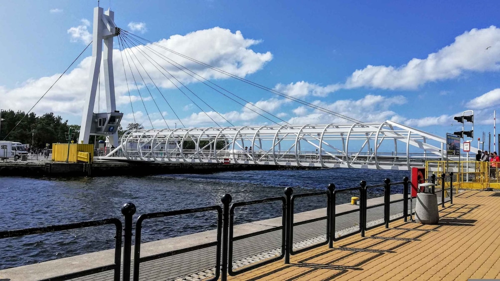 A modern cable-stayed bridge with a pedestrian walkway, a river below, and a wooden boardwalk with railings. 2