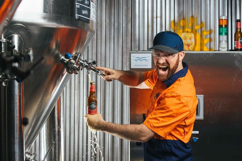 A person operating a tap in a brewery, holding a bottle of beer. 1