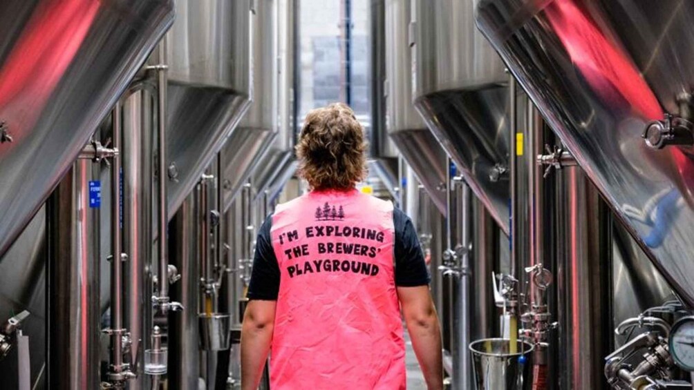 A person wearing a pink vest with text, walking through a corridor with industrial equipment. 2