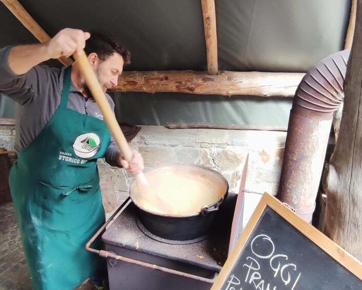A person cooking in a wood-fired oven, stirring a pot, with a chalkboard sign reading 'OGG PRAN'. 5