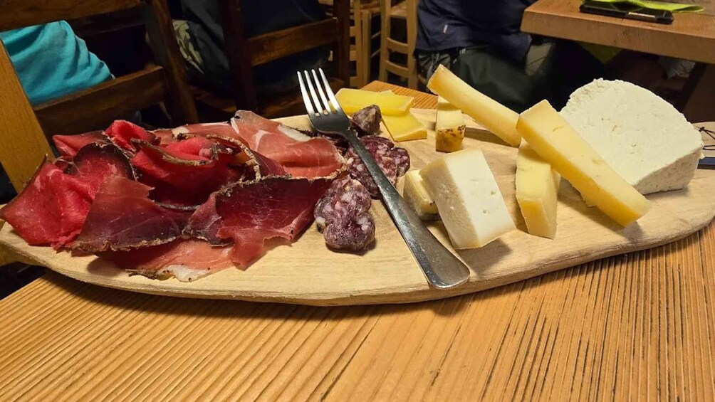 A wooden board with various cheeses, cured meats, and a knife. 3
