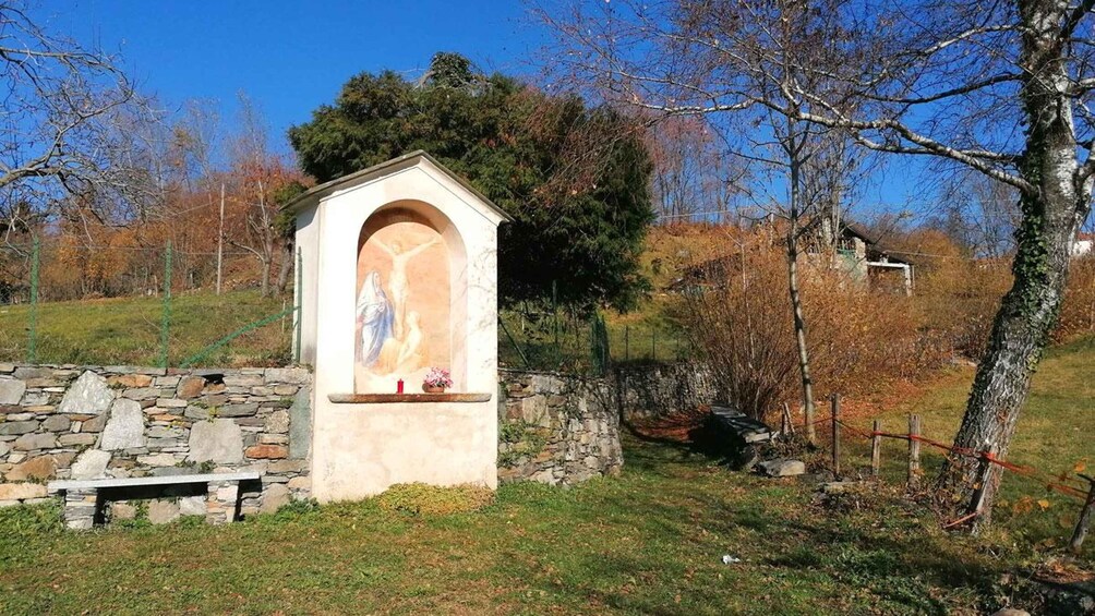 A stone chapel with a religious mural, surrounded by trees and a stone wall. 2