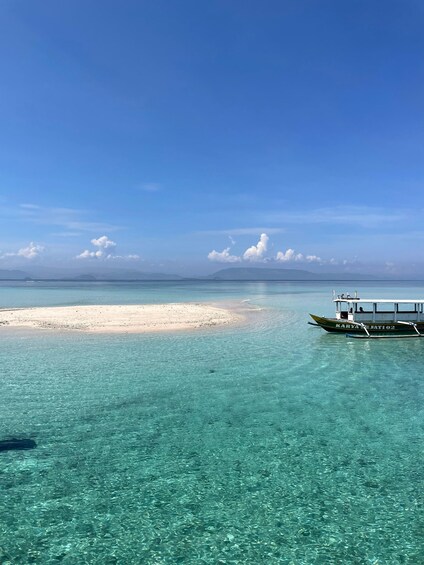 A boat named 'KARYA SEJATI 02' on clear turquoise waters, a sandy beach, and distant mountains under a blue sky. 3