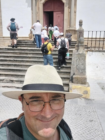 A person in a straw hat and backpack standing in front of a building with a red door and steps leading up to it. 4