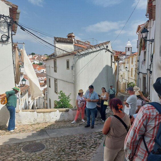A narrow street with cobblestone pavement, white buildings with red-tiled roofs, and a group of people standing and conversing. 3
