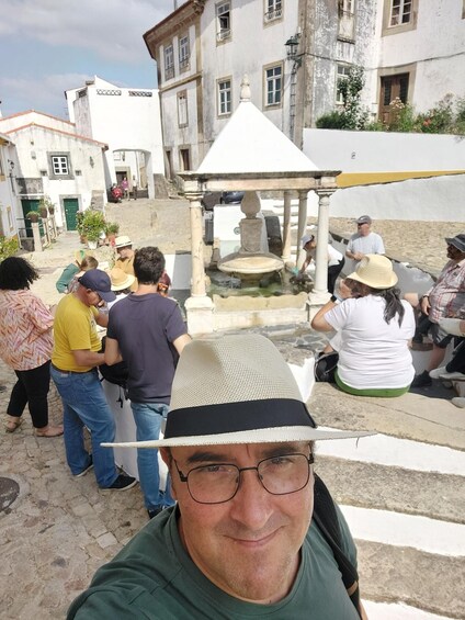 A group of people gathered around a fountain in a square with historic buildings in the background. 1